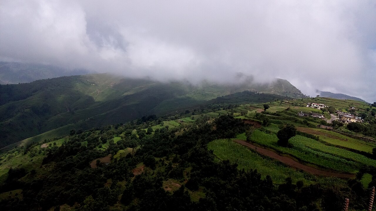 Clouds over green hills and scattered buildings at Chakrata