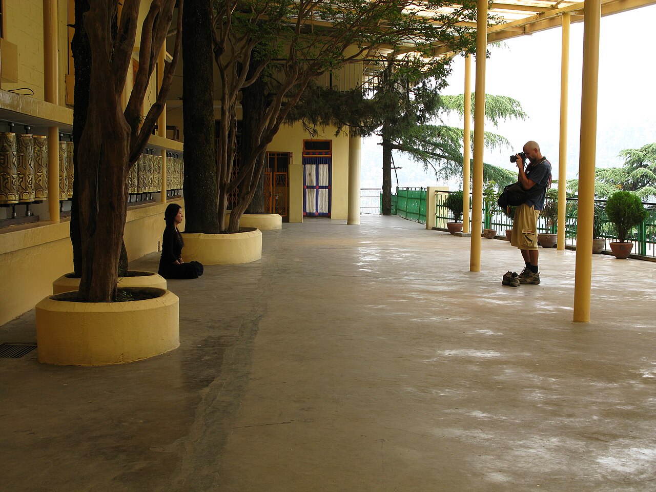 Visitors and prayer wheels in a shaded monastery courtyard in McLeodganj